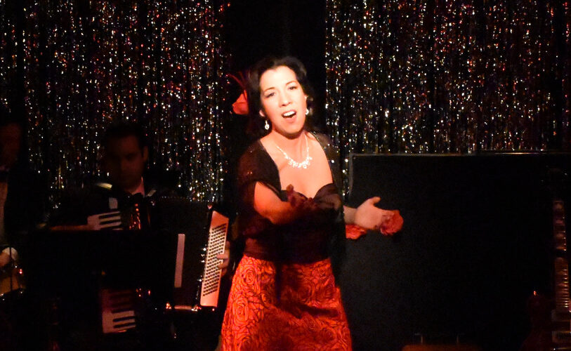A woman passionately singing on stage with a glittery backdrop.